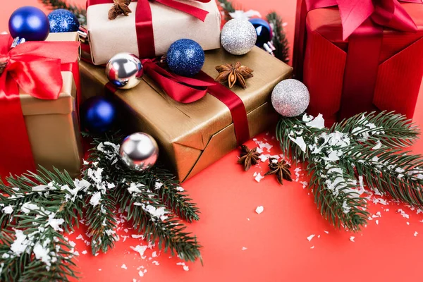 Gifts with baubles, anise stars, pine branches and artificial snow on red background — Stock Photo