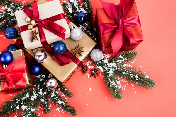 Vue du dessus des cadeaux avec des boules, des étoiles d'anis, des branches de pin et de la neige artificielle sur fond rouge — Photo de stock