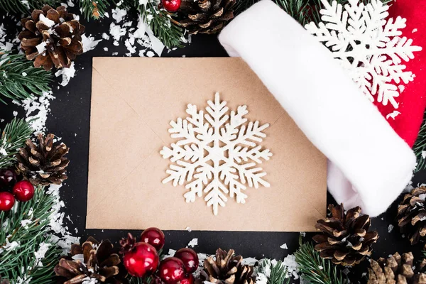 Draufsicht auf dekorative Schneeflocken auf Umschlag in der Nähe von Tannenzapfen, rote Perlen und Kunstschnee auf schwarzem Hintergrund — Stockfoto