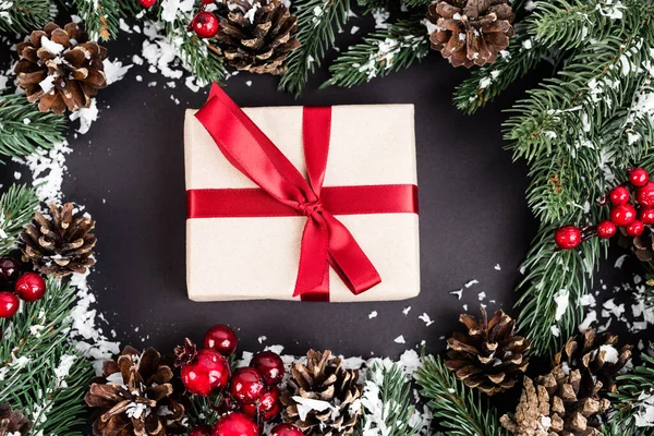 Vista dall'alto della confezione regalo vicino a rami di abete rosso, pigne e perline rosse su sfondo nero — Foto stock