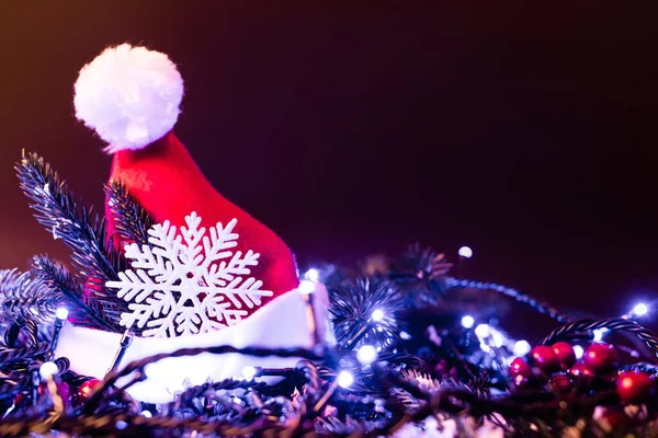 Oberflächenebene Weihnachtsmütze mit dekorativen Schneeflocken, Tannenzweigen und Weihnachtsbeleuchtung, Neujahrskonzept — Stockfoto