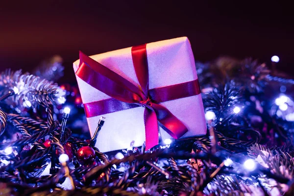 Nivel superficial de la pequeña caja de regalo cerca de ramas de pino con luces de Navidad en el fondo, concepto de año nuevo - foto de stock