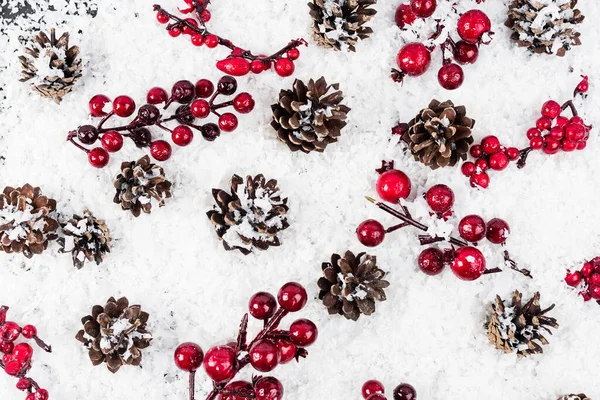 Vista superior de conos de pino y ramas con cuentas rojas sobre fondo texturizado blanco, concepto de año nuevo - foto de stock