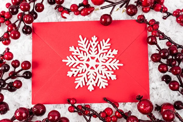 Top view of decorative snowflake on red envelope near branches with artificial berries on white textured background, new year concept — Stock Photo