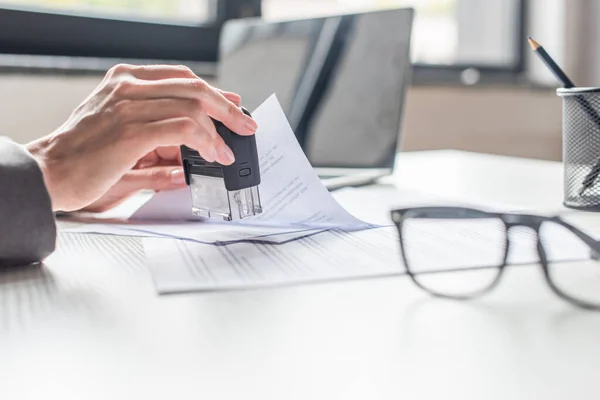 Cropped view of businesswoman putting stamp in document at workplace on blurred background — Stock Photo