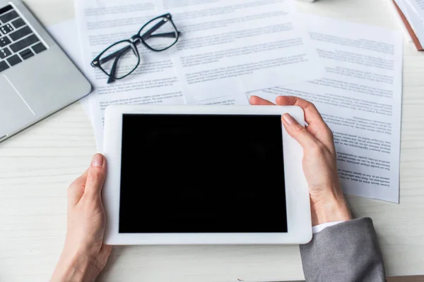 Vista cortada de empresária segurando tablet digital com tela em branco perto de documentos e óculos no local de trabalho — Fotografia de Stock