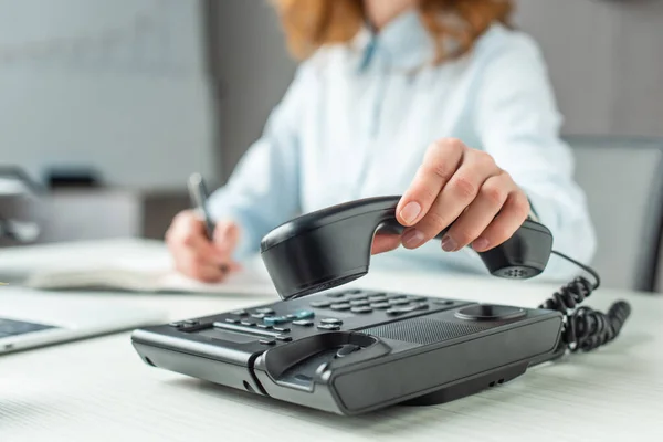 Vue recadrée de femme d'affaires mettant combiné sur téléphone fixe sur le lieu de travail sur fond flou — Photo de stock