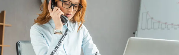 Femme d'affaires rousse parlant sur téléphone fixe avec tableau à feuilles floues sur fond, bannière — Photo de stock