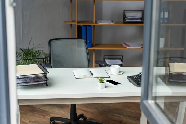 Interior do escritório com mesa, cadeira de escritório e prateleiras com janela embaçada em primeiro plano — Fotografia de Stock