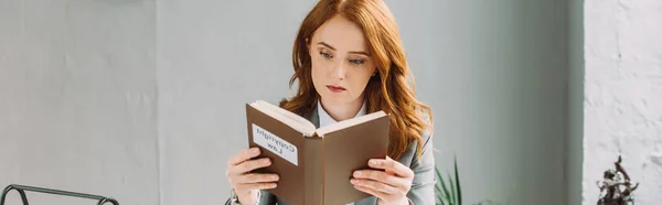 Concentrated redhead lawyer looking at book with copyright law lettering in office, banner — Stock Photo