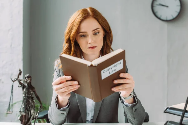 Avocate focalisée livre de lecture avec le droit d'auteur lettrage près de la figurine est au bureau sur fond flou — Photo de stock