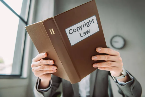 Buch mit urheberrechtlichem Schriftzug verhüllt Gesicht einer Rechtsanwältin auf verschwommenem Hintergrund — Stockfoto
