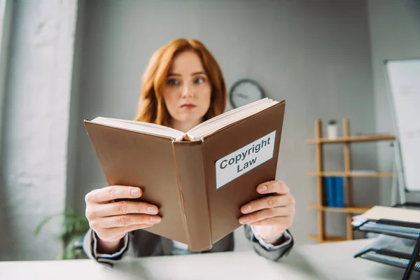 Low angle view of book with copyright law lettering in hands of female lawyer sitting at workplace on blurred background — Stock Photo