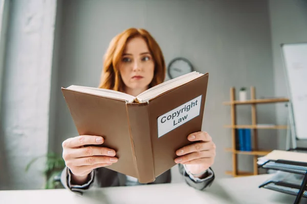 Низький кут зору на книгу з авторським правом в руках жінки-юриста, що сидить на робочому місці на розмитому тлі — стокове фото