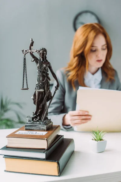 Themis Figur auf Bücherstapel auf dem Tisch mit verschwommener Anwältin im Hintergrund — Stockfoto