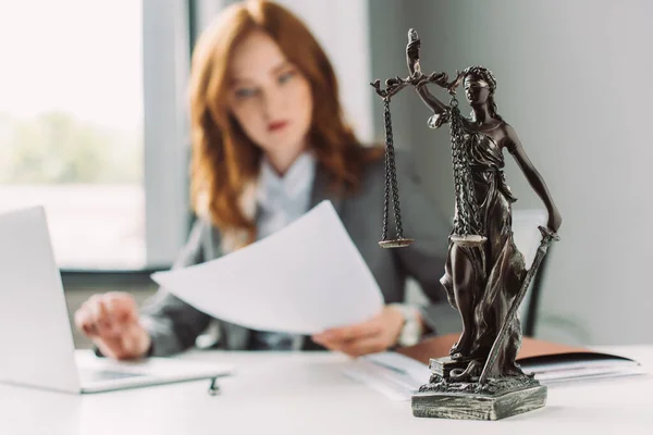 Themis Figur auf dem Tisch mit verschwommenem Anwalt, der am Hintergrund arbeitet — Stockfoto