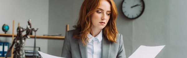 Redhead female lawyer looking at paper sheet with blurred themis figurine on foreground, banner — Stock Photo