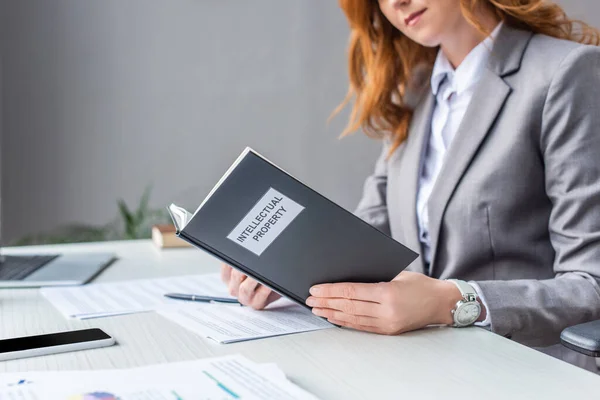 Ausgeschnittene Ansicht einer Rechtsanwältin mit Buch mit Schriftzug zum geistigen Eigentum am Arbeitsplatz auf verschwommenem Hintergrund — Stockfoto