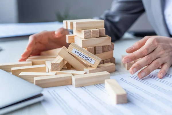 Cropped view of lawyer holding hands near blocks wood game construction with copyright lettering collapsing on blurred background — Stock Photo