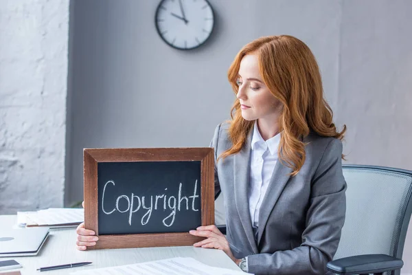 Женщина-юрист показывает доску с надписью авторского права, сидя на рабочем месте на размытом фоне — стоковое фото