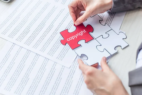 Cropped view of female lawyer putting red jigsaw puzzle with copyright lettering on table with documents — Stock Photo