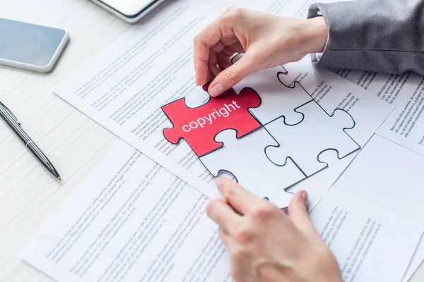 Vista recortada de la abogada poniendo rompecabezas rojo con letras de copyright en el lugar de trabajo con hojas de papel - foto de stock