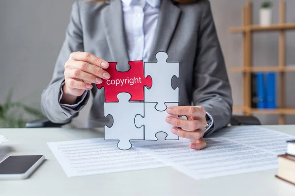 Ausgeschnittene Ansicht eines Anwalts, der Puzzles mit urheberrechtlichen Schriftzügen zeigt, während er am Arbeitsplatz auf verschwommenem Hintergrund sitzt — Stockfoto