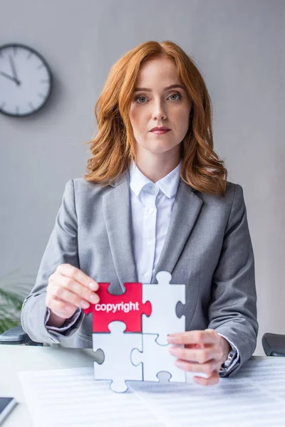 Serious lawyer looking at camera, while showing jigsaw puzzles with copyright lettering at workplace on blurred background — Stock Photo