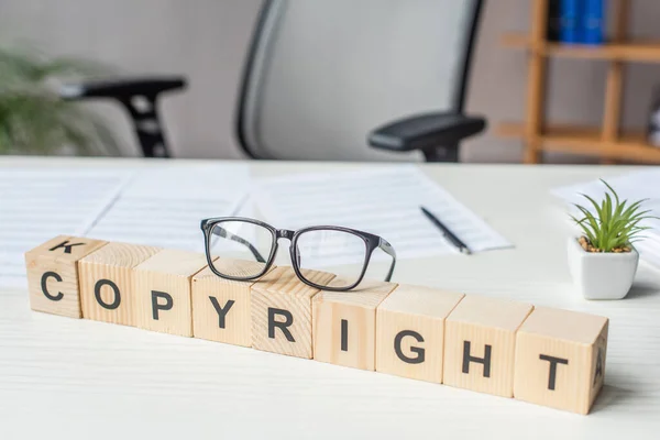 Close up of eyeglasses on wooden cubes with copyright lettering with blurred workplace on background — Stock Photo