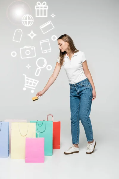 Mujer joven con tarjeta de crédito cerca de las bolsas de la compra y la ilustración en gris, concepto de viernes negro - foto de stock