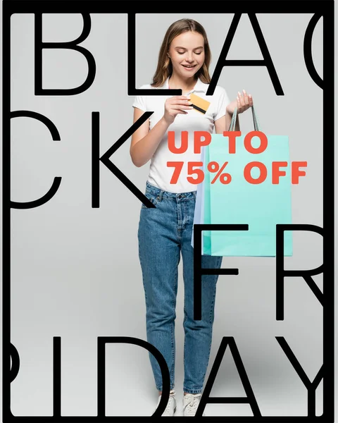 Mujer alegre sosteniendo la tarjeta de crédito y mirando las bolsas de compras azules cerca de letras viernes negro en gris - foto de stock