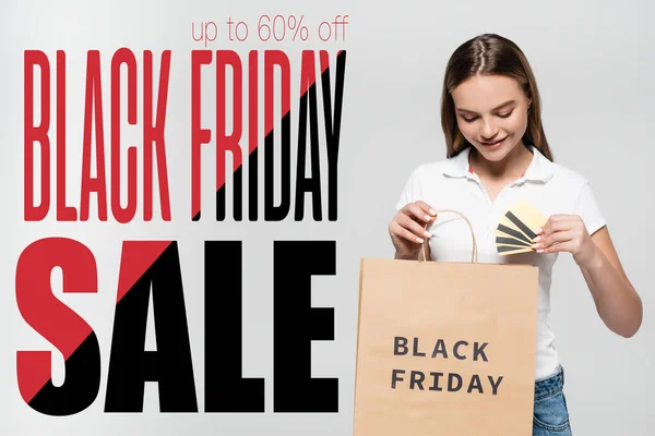 Freudige Frau mit Kreditkarte und Blick auf Einkaufstasche in der Nähe von Black Friday Sale Schriftzug auf grau — Stockfoto