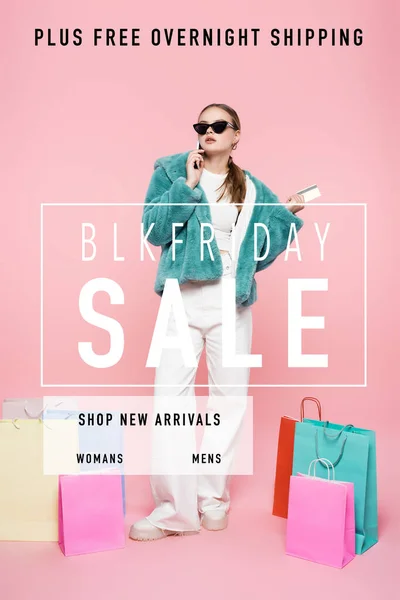 Stylische Frau mit Sonnenbrille, die mit Smartphone spricht und Kreditkarte in der Nähe von Einkaufstaschen hält und den Schriftzug blk Friday Sale auf rosa — Stockfoto