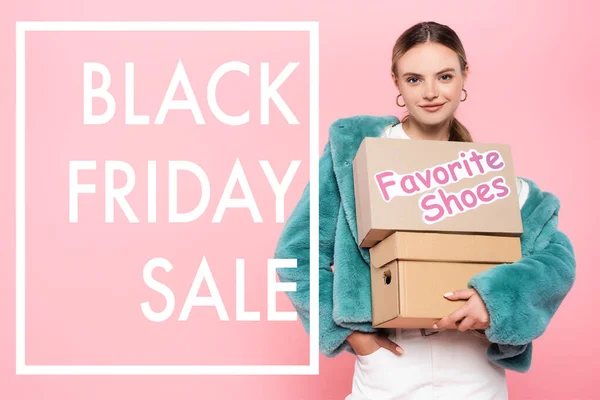 Piacere donna in occhiali da sole in possesso di scatole con scarpe preferite vicino Venerdì nero vendita lettering su rosa — Foto stock