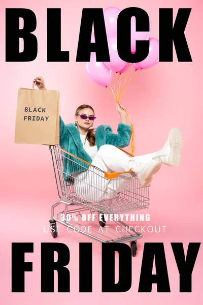 Stylish woman in sunglasses sitting in cart with shopping bags and holding balloons near black friday lettering and tag on pink — Stock Photo