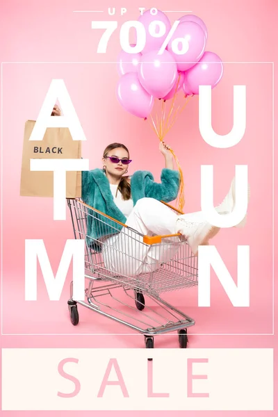 Стильна жінка в сонцезахисних окулярах сидить у візку з сумками для покупок і тримає повітряні кулі біля осіннього розпродажу написи та теги на рожевому — стокове фото