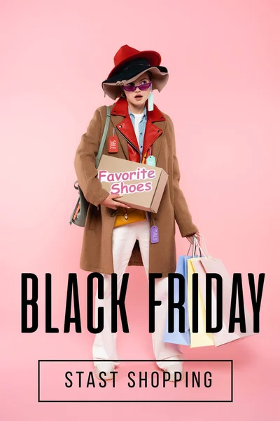 Surprised woman in sunglasses and hats with sale tags holding box with favorite shoes and shopping bags near black friday lettering on pink — Stock Photo