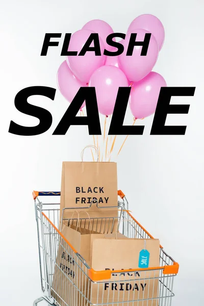 Bolsas de compras con viernes negro en el carrito con globos de color rosa cerca de la venta flash de letras en blanco — Stock Photo