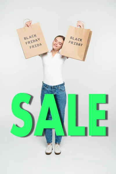 Donna soddisfatto con gli occhi chiusi tenendo borse della spesa vicino Venerdì nero vendita lettering su bianco — Foto stock