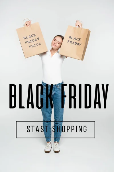 Pleased woman with closed eyes holding shopping bags near black friday stast shopping lettering on white — Stock Photo