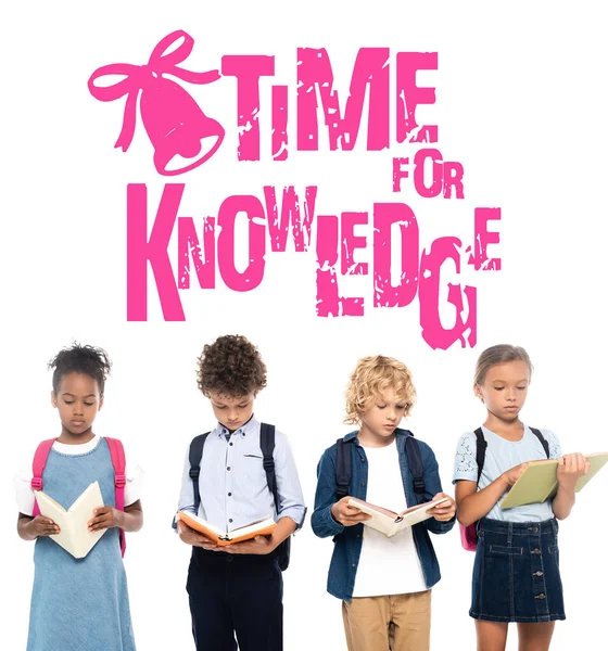 Multicultural schoolkids with backpacks reading books near time for knowledge lettering on white — Stock Photo