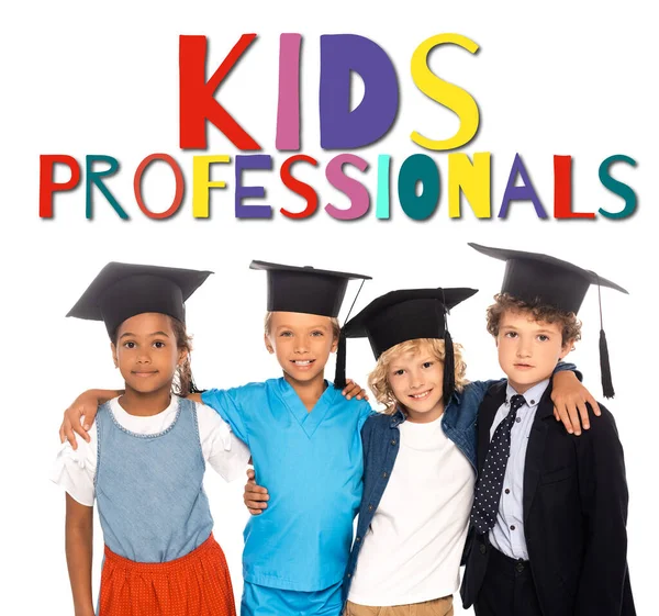 Multicultural kids in graduation caps dressed in costumes of different professions near kids professionals lettering on white — Stock Photo