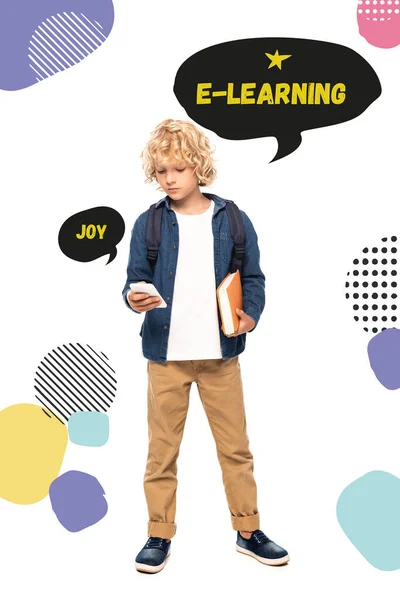 Blonde schoolboy holding book and using smartphone near speech bubbles with joy and e-learning words on white — Stock Photo