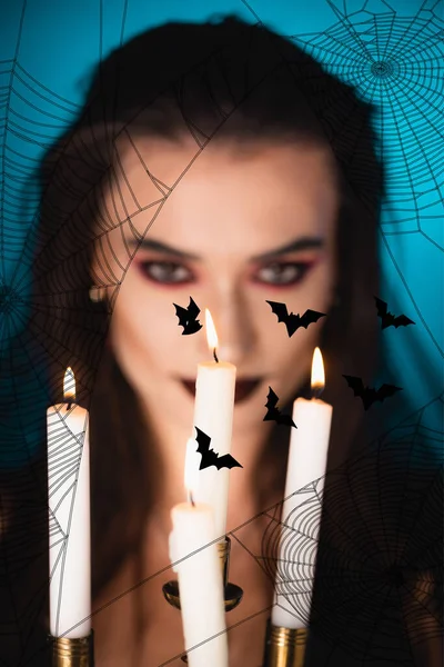 Burning candles near young woman with black makeup near bats illustration on blue — Stock Photo