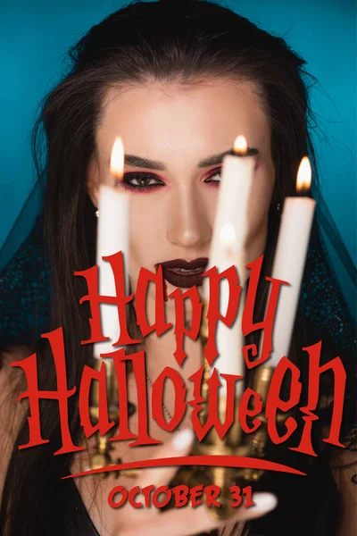 Young woman in veil with blood on face near burning candles and happy halloween lettering on blue — Stock Photo