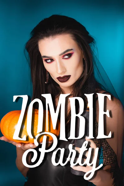 Young pale woman with black makeup and veil holding burning candle and pumpkin near zombie party on blue — Stock Photo