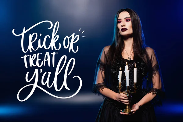 Woman in black dress and veil holding burning candles near trick or treat lettering on blue — Stock Photo