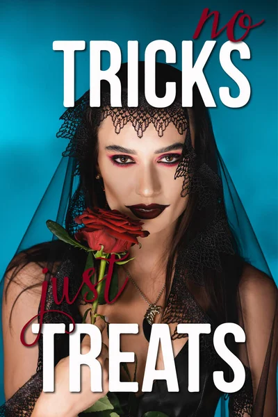 Evil woman with black makeup and dark veil holding rose near no tricks just treats lettering on blue — Stock Photo