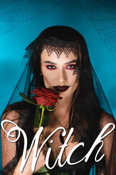 Femme maléfique avec maquillage noir et voile foncé tenant rose près de lettrage sorcière sur bleu — Photo de stock