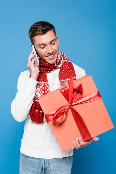 Homme souriant avec boîte cadeau, parlant sur smartphone isolé sur bleu — Photo de stock